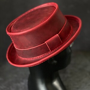 May include: A red leather fedora hat with a stitched brim and a leather band.
