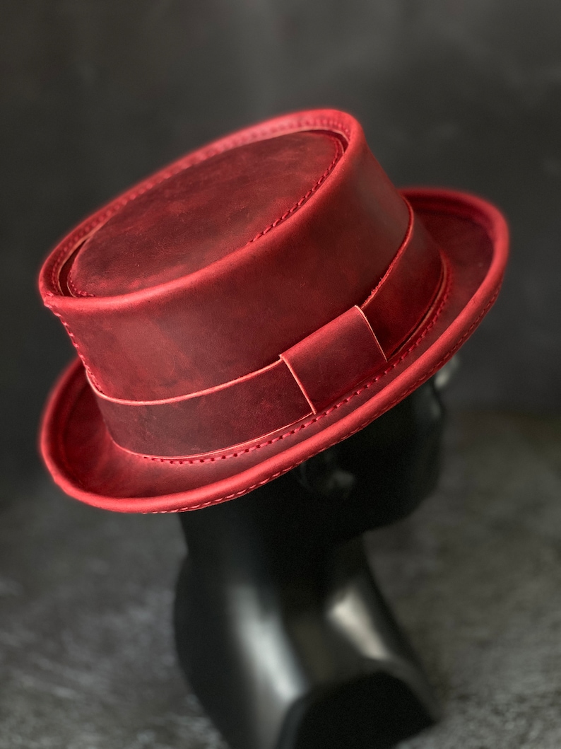 May include: A red leather fedora hat with a stitched brim and a leather band.