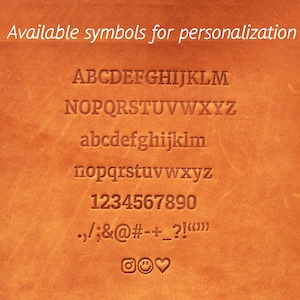 Puede incluir: Primer plano de una superficie de cuero marr&oacute;n con una lista de s&iacute;mbolos disponibles para la personalizaci&oacute;n. Los s&iacute;mbolos incluyen letras may&uacute;sculas y min&uacute;sculas, n&uacute;meros, signos de puntuaci&oacute;n y algunos emojis.