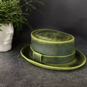 May include: A green leather fedora hat with a wide brim and a stitched band around the crown.