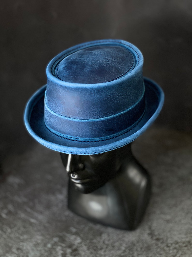May include: A blue leather fedora hat with a wide brim and a stitched band around the crown.