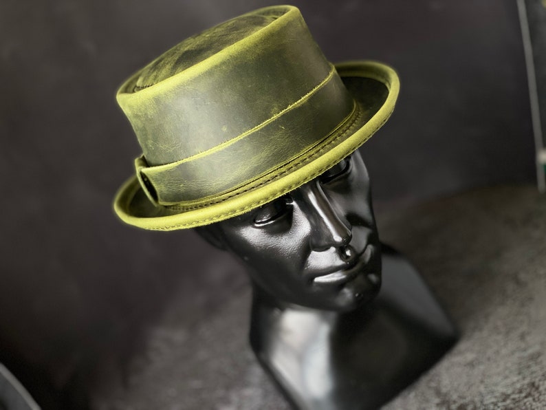 May include: A green leather fedora hat with a wide brim and a band around the crown.