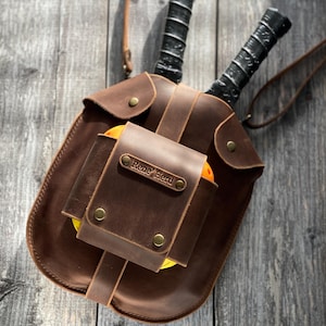 Puede incluir: Una bolsa de cuero marr&oacute;n con una etiqueta de nombre personalizada que dice "Rene' Bird". La bolsa tiene dos raquetas de paddleball negras en su interior y una pelota de paddleball amarilla.