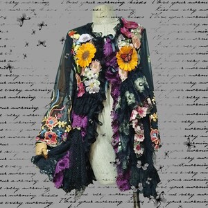 May include: A black long-sleeve jacket featuring sheer fabric, layered lace, and ruffles. The garment is decorated with various colorful floral appliques, including large yellow sunflowers, pink blossoms, and embroidered butterflies.