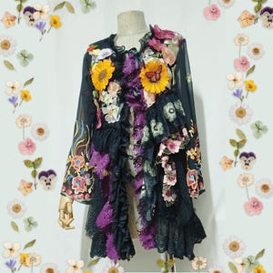 May include: A black long-sleeve jacket featuring layered ruffles, purple lace trim, and various floral appliques including yellow sunflowers and a butterfly. The garment has a sheer fabric base with intricate embroidery and decorative ribbons.