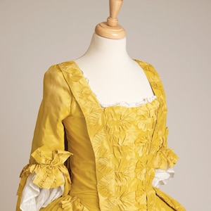 May include: A yellow silk dress with a fitted bodice and a full skirt. The bodice is decorated with intricate floral embroidery. The skirt is gathered and has a ruffled hem.