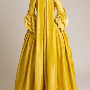 May include: A yellow gown with long sleeves and a ruffled trim. The gown has a fitted bodice and a full skirt.