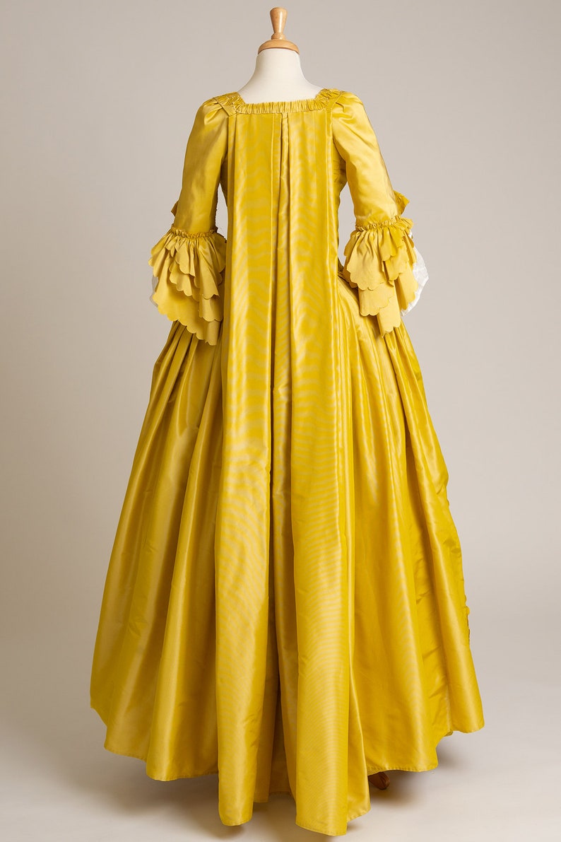 May include: A yellow gown with long sleeves and a ruffled trim. The gown has a fitted bodice and a full skirt.
