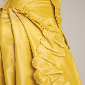 May include: A yellow skirt with a ruffled trim. The skirt is made of a smooth, silky fabric.