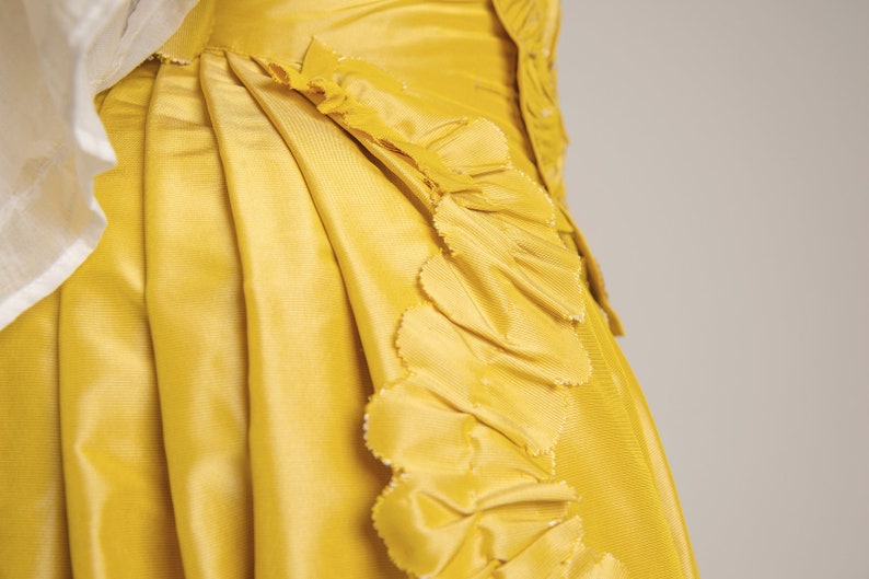 May include: A yellow skirt with a ruffled trim. The skirt is made of a smooth, silky fabric.