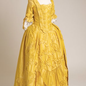 May include: A yellow silk dress with a fitted bodice and a full skirt. The dress is decorated with intricate floral embroidery and ruffles.