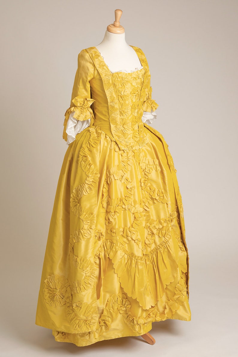 May include: A yellow silk dress with a fitted bodice and a full skirt. The dress is decorated with intricate floral embroidery and ruffles.