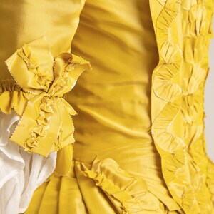 May include: A yellow silk dress with a ruffled trim and a decorative pattern on the back.