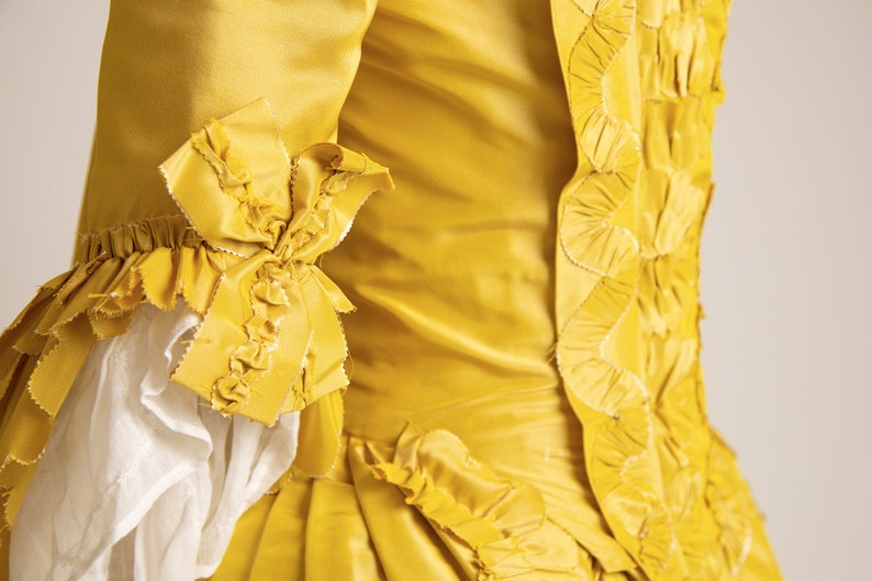 May include: A yellow silk dress with a ruffled trim and a decorative pattern on the back.
