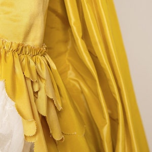 May include: A yellow dress with a ruffled hem and a flowing skirt. The dress is made of a soft, silky fabric.