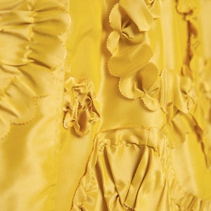 May include: Close-up of a yellow fabric with a textured, ruffled design. The fabric is made of multiple layers of material, creating a three-dimensional effect.