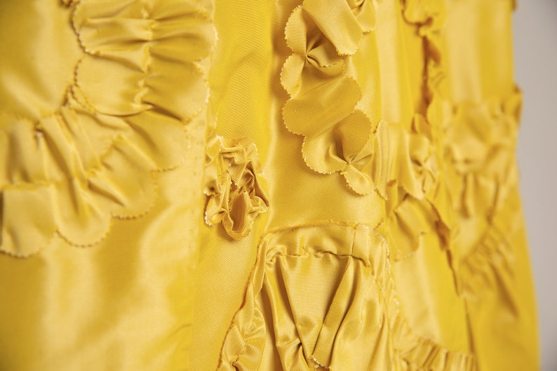 May include: Close-up of a yellow fabric with a textured, ruffled design. The fabric is made of multiple layers of material, creating a three-dimensional effect.