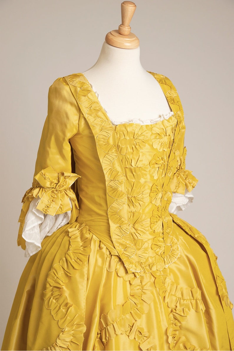 May include: A yellow silk dress with a fitted bodice and a full skirt. The bodice is decorated with intricate floral embroidery. The skirt is gathered and has a ruffled hem.
