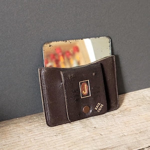 Peut inclure: Un miroir de poche compact en cuir marron vintage avec un miroir rectangulaire. Le compact a une fermeture à bouton-pression et un emblème doré avec la lettre "J". Les mots "Hair Grips" sont imprimés sur le devant.