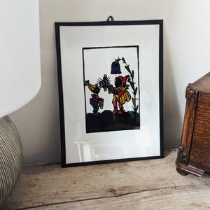 May include: A framed black and white illustration of two figures in a woodland setting. The figures are wearing colourful clothing and are holding a flower. The illustration is set against a white background.