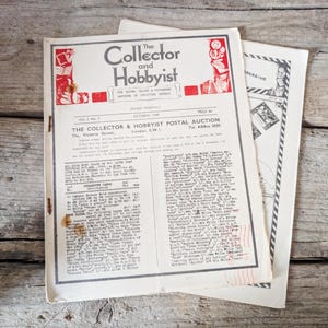 Pode incluir: Revista vintage "The Collector and Hobbyist" de outubro de 1949, com um leilão postal. A capa é branca com texto e ilustrações em vermelho e preto. A revista está aberta, revelando texto detalhado.