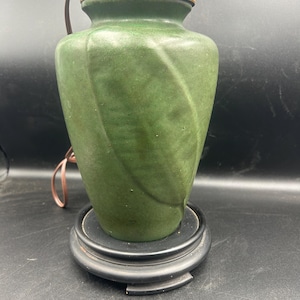 May include: A green ceramic table lamp with a leaf design. The lamp has a brass base and a black wooden base.