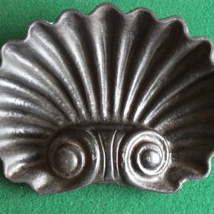 May include: A black cast iron decorative shell with a scalloped edge and two decorative scrolls at the bottom.