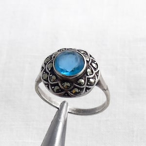 May include: A silver ring with a blue gemstone surrounded by a halo of marcasite stones.