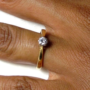 Pu&ograve; includere: Un anello semplice in oro con un'unica piccola pietra rotonda trasparente.