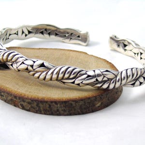 May include: Silver bangle bracelet with a braided design featuring a leaf pattern.