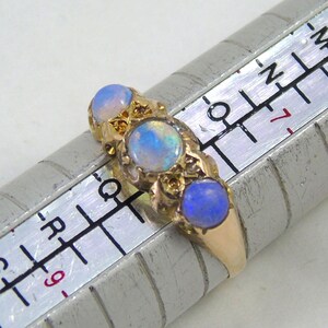 May include: A gold ring featuring three oval opals. The opals display a blue and white iridescent sheen. The ring is placed on a ring sizer.