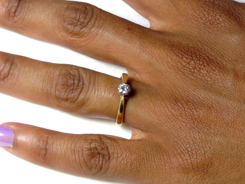 Pu&ograve; includere: Un anello semplice in oro con un'unica piccola pietra rotonda trasparente.