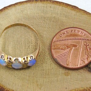 May include: A gold ring featuring three opals and a penny coin. The ring has an ornate design with the opals set in a row. The copper penny coin displays the words "ONE PENNY".