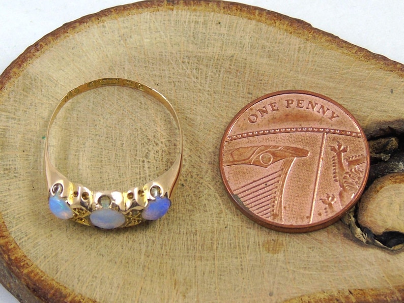 May include: A gold ring featuring three opals and a penny coin. The ring has an ornate design with the opals set in a row. The copper penny coin displays the words "ONE PENNY".