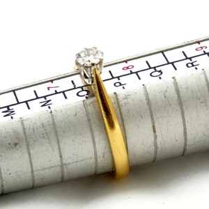 Pu&ograve; includere: Un anello con fascia in oro con un solo diamante rotondo incastonato a griffe. L'anello &egrave; misurato su un calibratore per anelli, che mostra una misura 7.