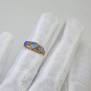 May include: A gold ring with three oval opals. The opals are set in a decorative band. The ring is displayed against a white background.