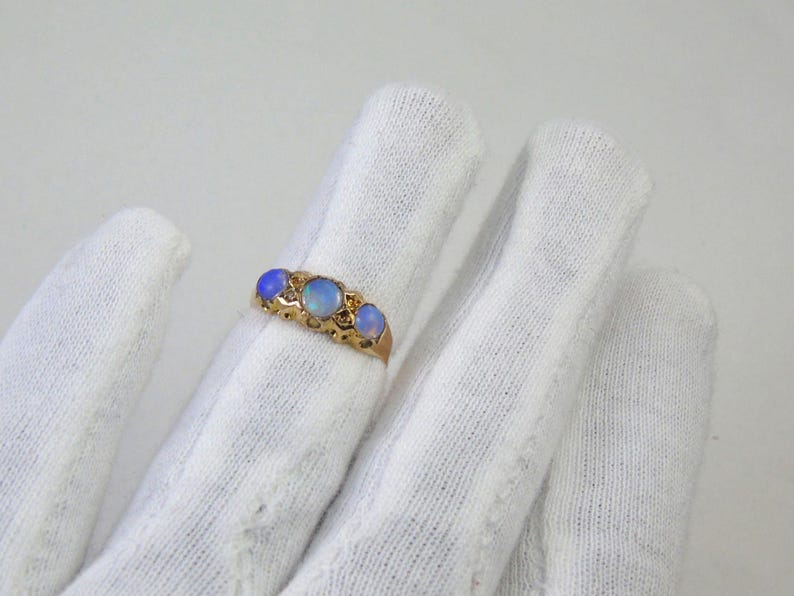 May include: A gold ring with three oval opals. The opals are set in a decorative band. The ring is displayed against a white background.