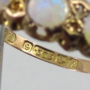 May include: Close-up of a gold ring with three opalescent stones. The ring has a detailed design and is stamped with hallmarks including "9 .375". The ring is a piece of jewellery.