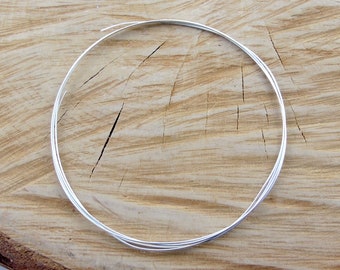 May include: A coil of silver wire on a wooden surface.