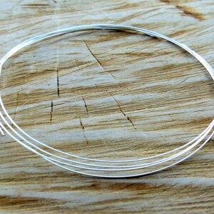 May include: A close-up of a silver wire coil on a wooden surface. The wire is thin and shiny, and it is coiled into a tight circle.