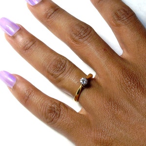 Pu&ograve; includere: Un anello d'oro con una singola pietra preziosa trasparente incastonata a griffe. L'anello &egrave; su un dito.