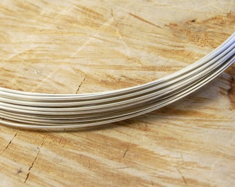 May include: A coil of silver wire, approximately 10 feet long, is shown on a wooden surface. The wire is shiny and has a smooth finish.