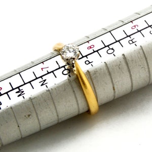 Pu&ograve; includere: Un anello d'oro con un solo diamante trasparente incastonato a griffe. L'anello viene misurato su un calibratore di anelli in metallo, che indica che la misura dell'anello &egrave; 7.
