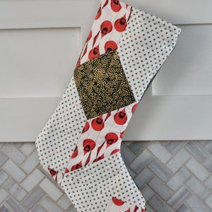 May include: A red and white Christmas stocking with a black and gold geometric pattern. The stocking is made of fabric and has a quilted design.