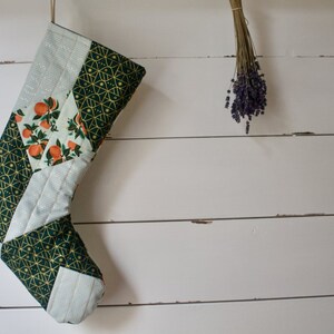 May include: A green and white Christmas stocking with a geometric pattern and orange citrus fruit design.
