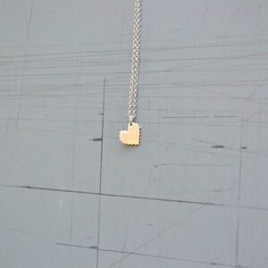 May include: A silver chain necklace with a small gold heart pendant. The heart is made of small squares, giving it a pixelated look.