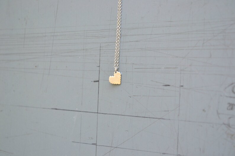May include: A silver chain necklace with a small gold heart pendant. The heart is made of small squares, giving it a pixelated look.