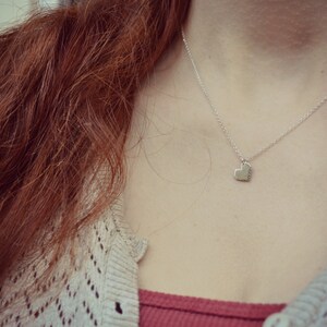 May include: A silver necklace with a heart pendant. The necklace is worn by a person with long, red hair.