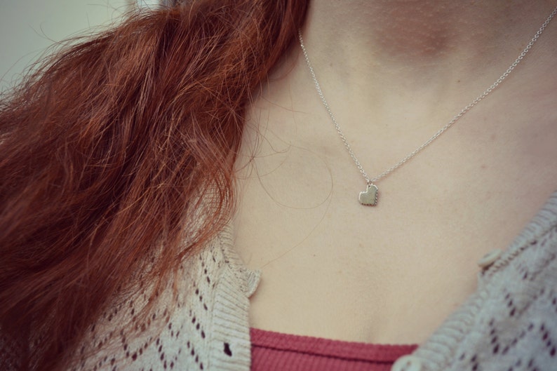 May include: A silver necklace with a heart pendant. The necklace is worn by a person with long, red hair.