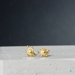 May include: A pair of gold turtle stud earrings. The earrings are small and delicate, and they are perfect for adding a touch of whimsy to any outfit.